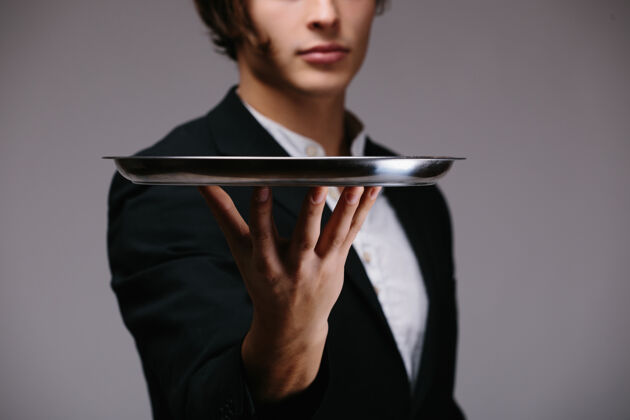 服务员一个穿着西装的年轻人拿着一个空盘子孤立在白墙上年轻餐饮服务