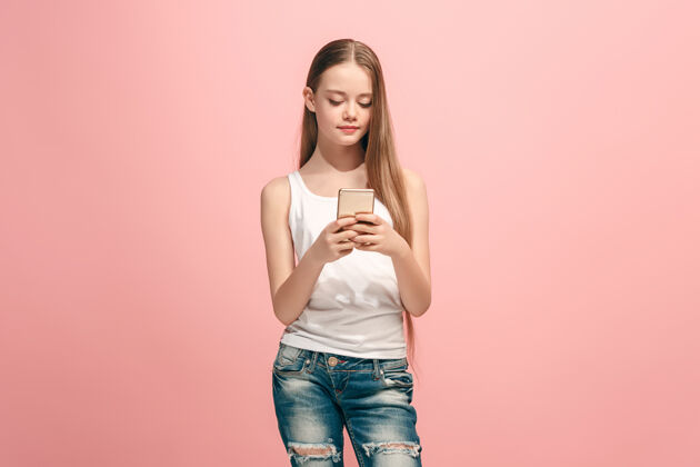 漂亮快乐的少女站着 微笑着用手机在时尚的粉红色工作室成人学生生活方式