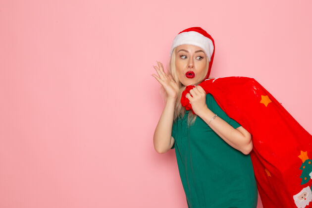 圣诞老人正面图年轻女性提着红包在粉色墙上送礼物模型圣诞新年照片彩色圣诞老人假期喜剧演员娱乐美丽