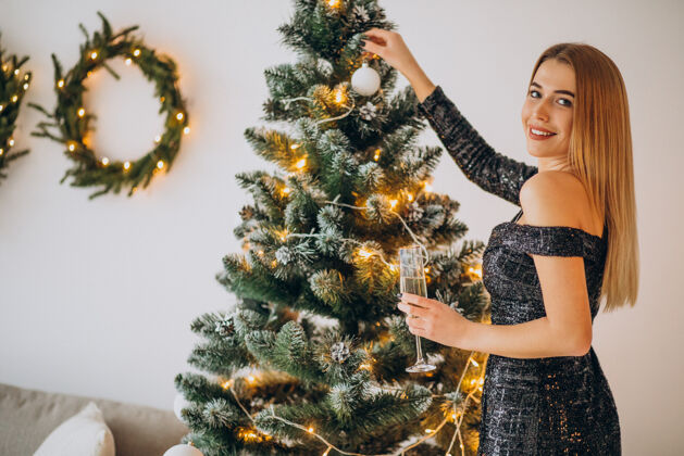 葡萄酒年轻女子在圣诞树旁喝香槟时尚女性庆祝