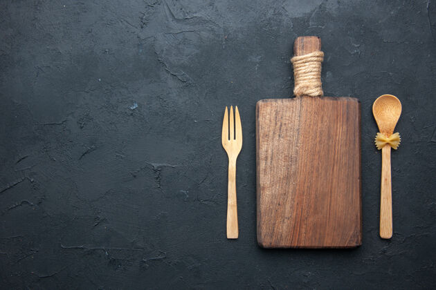 黑的顶视图木制服务板木制勺子和叉子在黑暗的桌子上复制的地方木槌叉子金属