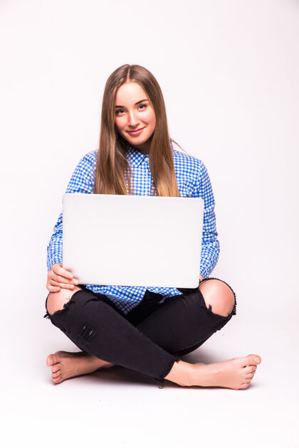微笑年轻随意的女人坐下来微笑着拿着笔记本电脑隔离在白墙上快乐互联网笔记本电脑