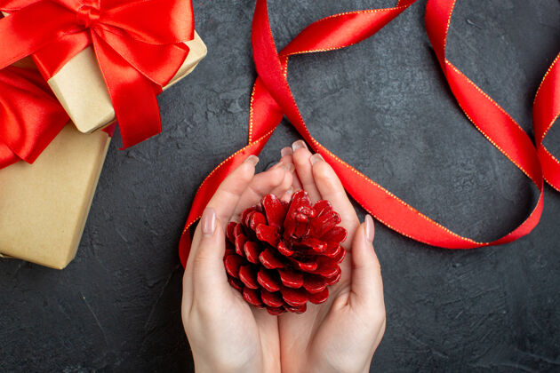 圣诞节上图中 手拿着一个针叶树圆锥体 在黑暗的背景下是一份美丽的礼物玫瑰胡椒花瓣
