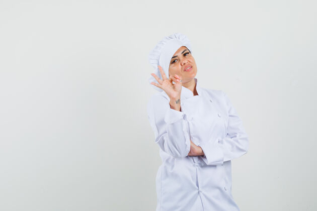 专业身着白色制服的女厨师摆出ok的姿势 看上去很自信工作烹饪食品