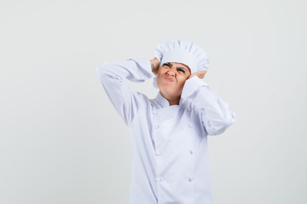 专业穿着白色制服的女厨师手捂着耳朵 看起来很恼火柜台工作烦恼