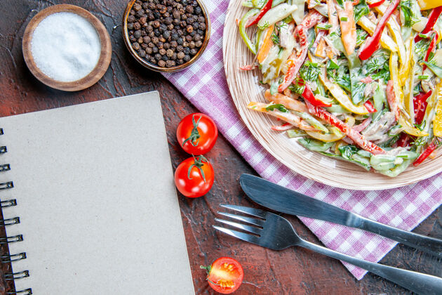 肉顶视图蔬菜沙拉在盘子上桌布叉子和刀子盐和黑胡椒西红柿笔记本在深红色的桌子上胡椒笔记本沙拉