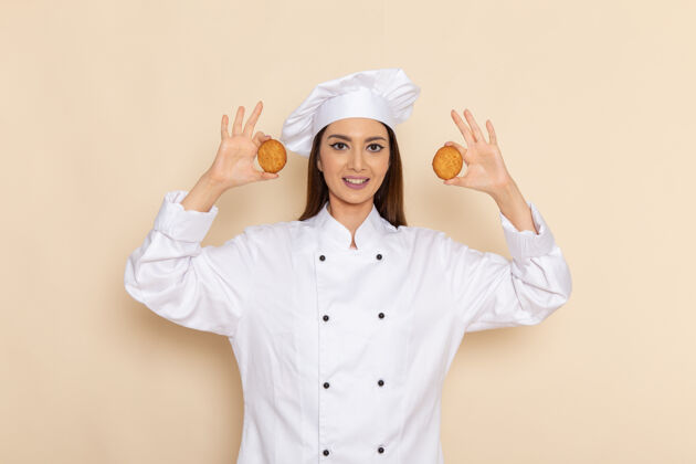 烹饪身穿白色厨师服的年轻女厨师正对着浅白的墙壁微笑着拿着饼干前面女性举行