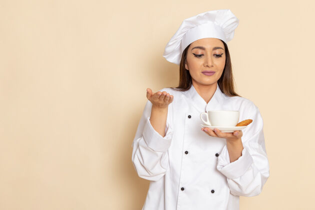 烹饪身穿白色厨师服的年轻女厨师正拿着咖啡站在浅白的墙上工作举行职业