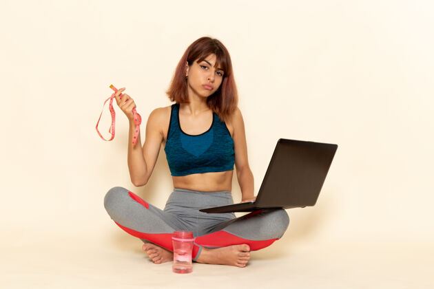 私人教练穿着蓝色衬衫 身体健康的年轻女性在浅白墙上使用笔记本电脑的前视图灯运动电脑