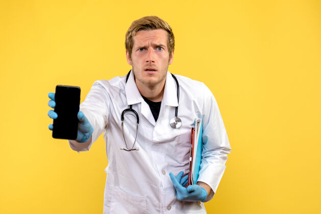 人正面图年轻男医生拿着手机 背景是黄色的健康医学人病毒持有男性电话