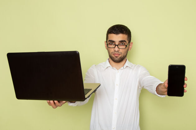 男人身穿白衬衫 手持笔记本电脑和电话的男办公室工作人员的正面图笔记本电脑办公室电话