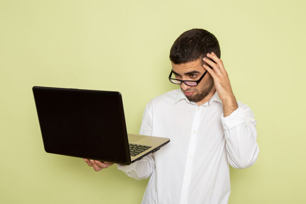 笔记本电脑身穿白衬衫的男办公室工作人员在浅绿色墙上使用笔记本电脑的正视图男性办公室前台
