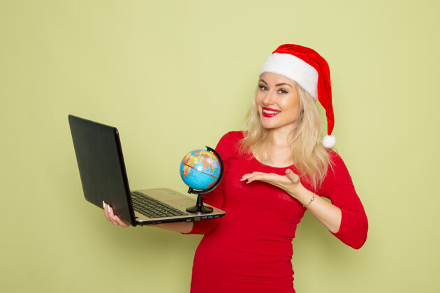 笔记本电脑正面图美丽的女性手持地球仪和笔记本电脑在绿色的墙上度假情感圣诞雪新年的颜色漂亮情感小