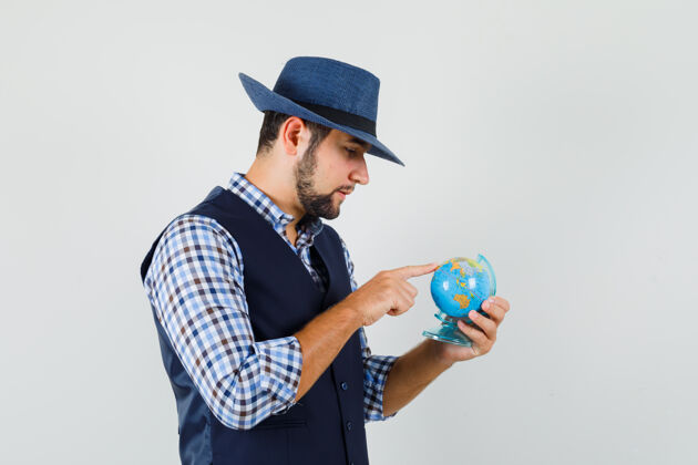 英俊年轻人穿着衬衫 背心 戴着帽子 神情沉思地选择着地球上的目的地目的地休闲衬衫