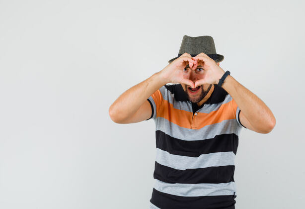 发型一个穿着t恤 戴着帽子的年轻人 展示着心形和可爱的表情 正面视图帽子男人自信