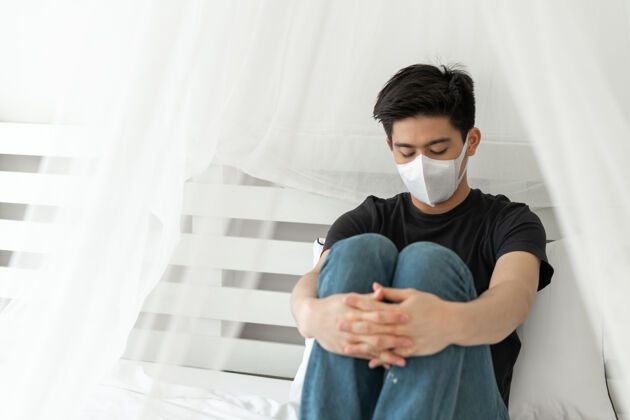 紧张亚洲男子戴口罩以防在检疫室因冠状病毒冠状病毒-19而感到头痛和咳嗽痛苦14天健康