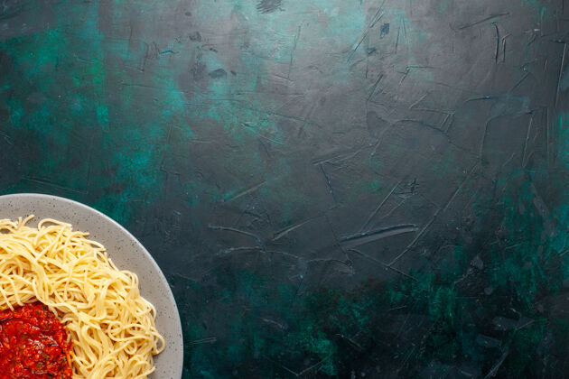 意大利面俯视图：深蓝色表面上有肉末和番茄酱的熟意大利面食面团酱汁图案