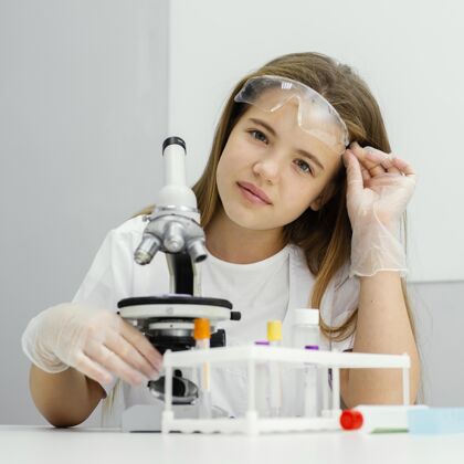 女孩年轻女科学家在使用显微镜时摆姿势的前视图知识实验室外套青年