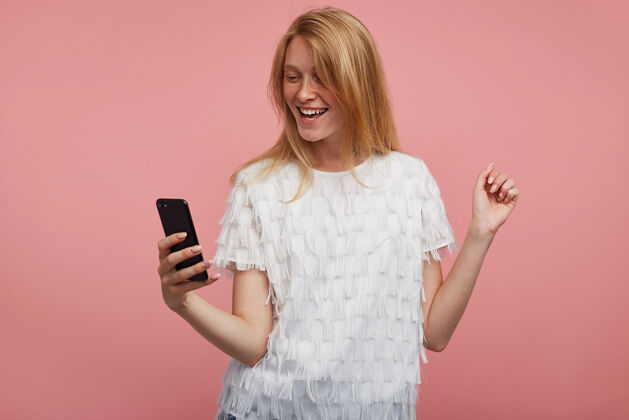 雀斑快乐的年轻漂亮的红发女性 随意的发型 手举着手机 拍着自己的照片 面带微笑 与粉色背景隔离站白色女性
