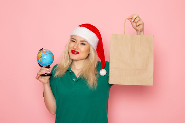圣诞节正面图年轻女性手持地球仪和圣诞礼物在粉红色墙上的照片模特妇女新年假期年轻的女性漂亮女人