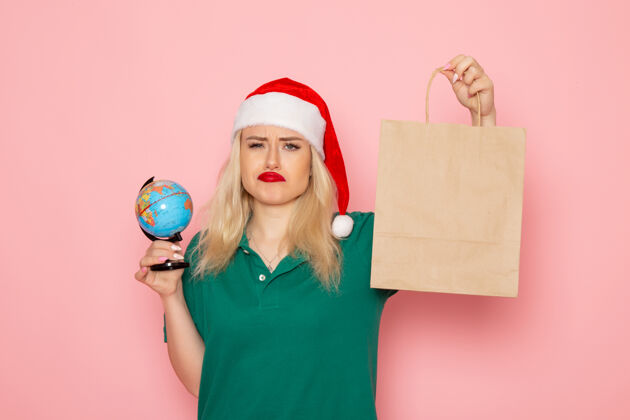 女人正面图年轻女性拿着地球仪和圣诞礼物在粉红色墙上的照片模特妇女新年假期风景圣诞节年轻的女性