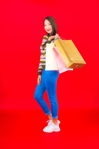 购物在红墙上画一幅美丽的亚洲年轻女子 带着五颜六色的购物袋买家付款促销