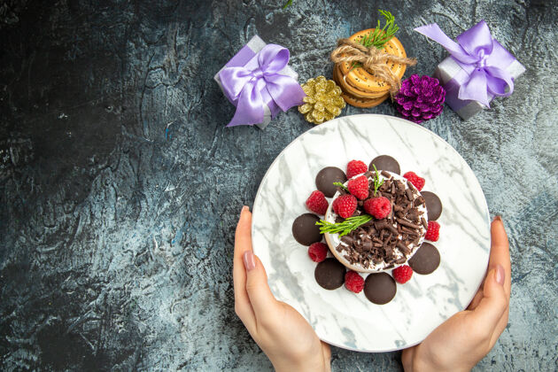 顶部俯瞰巧克力芝士蛋糕椭圆形盘子在女人手中圣诞礼物灰色表面免费空间花束插花景观