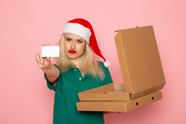 披萨正面图年轻女性手持银行卡和披萨盒在粉色墙上彩色节日圣诞照片工作服银行笔记本电脑盒子
