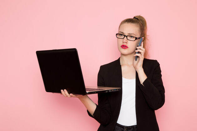 工人身穿黑色夹克的女上班族在浅粉色墙上手持和使用笔记本电脑的正面图办公室夹克业务