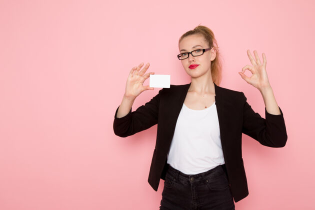 模特身穿黑色紧身夹克 手持白色塑料卡的女上班族在浅粉色墙上的正视图塑料办公室正面