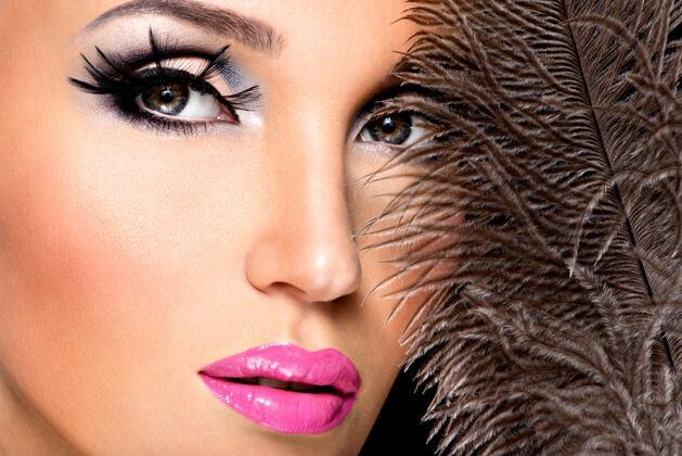 女性美丽的女人用明亮的专业化妆品和羽毛靠近脸模特女人皮肤