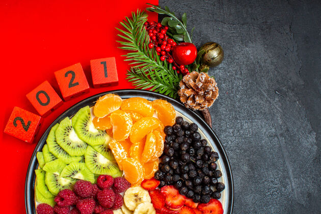 一半收集新鲜水果的半张照片在餐盘上装饰配件杉木枝和数字在黑色背景上的红色餐巾上晚餐盘新鲜饮食
