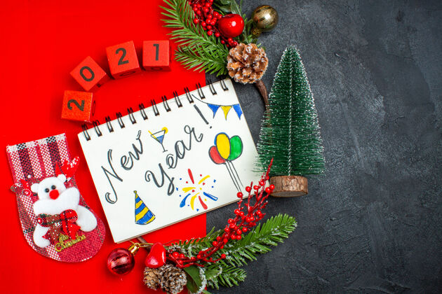 绘图上图是带有新年书写和图纸的螺旋笔记本装饰配件杉木树枝红色餐巾上的xsmas袜子编号和深色背景右侧的圣诞树冷杉圣诞节视图