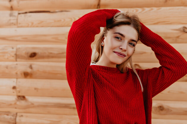 金发快乐的年轻金发女郎穿着时髦的红色毛衣在户外的木墙上摆姿势穿着时髦季节性服装的漂亮女孩微笑着户外长年轻
