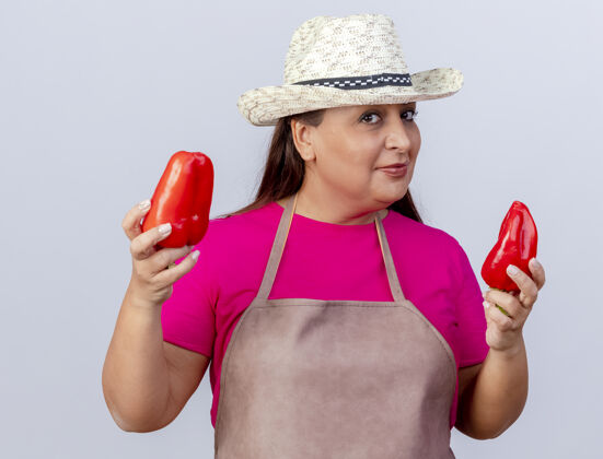 年龄穿着围裙 戴着帽子的中年园丁 手里拿着新鲜的红甜椒 站在白色的背景上 自信地微笑着看着镜头微笑红帽子