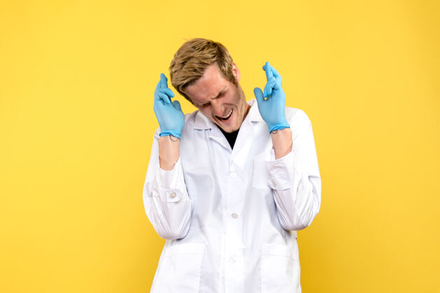 护士前视图年轻男性医生交叉手指在黄色背景人类冠状病毒-大流行医学视图男性衣服