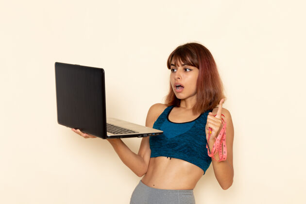 运动穿着蓝色衬衫 身体健康的年轻女性在浅白墙上使用笔记本电脑的前视图身体运动员笔记本电脑