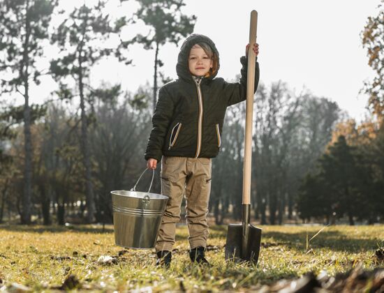 水平户外抱着水桶和铲子的小男孩的正面图种植庭院自然