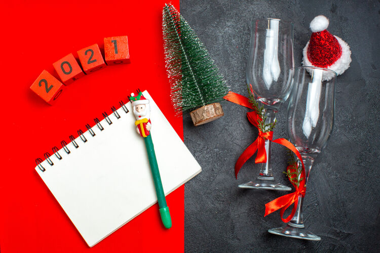 采购产品圣诞节上图为手持螺旋笔记本和圣诞树玻璃高脚杯的黑色和红色背景上的数字钢笔螺旋笔记本螺丝刀