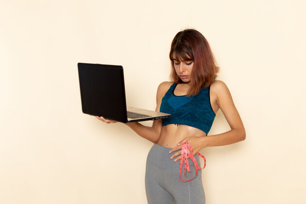 身体前视图中的年轻女性身体健康 穿着蓝色衬衫 将笔记本电脑放在白色墙上前面运动锻炼