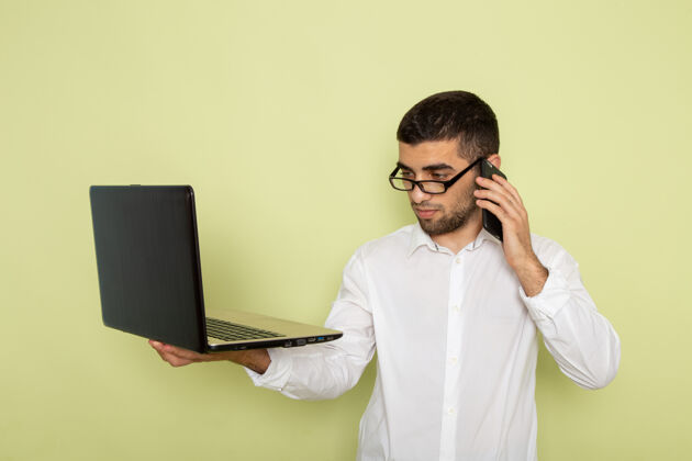 成人身穿白衬衫的男办公室工作人员手持笔记本电脑在绿色墙壁上打电话电话衬衫工作
