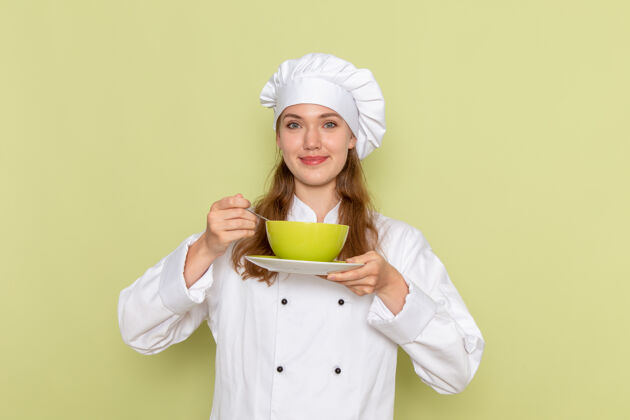 烹饪身着白色厨师服的女厨师正拿着绿色盘子站在绿色墙上厨师前面烹饪