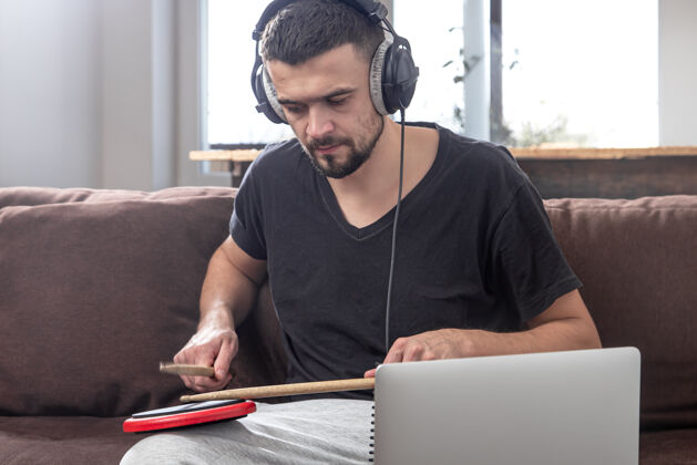 在家里一个男人打鼓 看着笔记本电脑屏幕在线音乐课 视频会议课的概念欧洲创意发挥