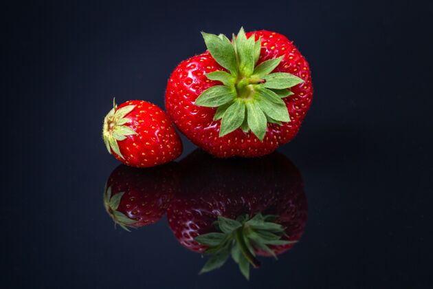 甜点两个红色的克罗地亚草莓在黑色反射面水平拍摄葡萄干立方体素食