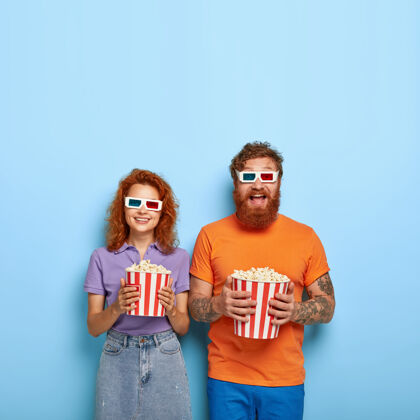 搞笑在电影院娱乐的快乐红发男朋友和女朋友的镜头 戴3d眼镜 看搞笑喜剧 从篮子里吃爆米花 一起度过空闲时间 享受搞笑电影电影站美味
