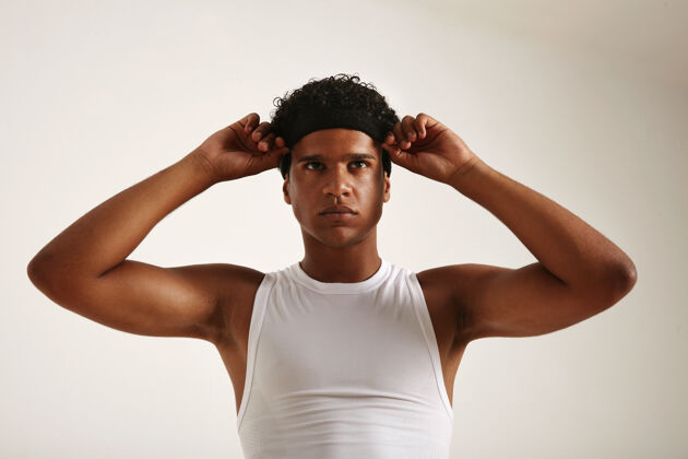 比赛肌肉发达的非洲裔美国运动员 穿着白色篮球衫 调整着他的黑色头带 看上去很轻微运动室内运动员