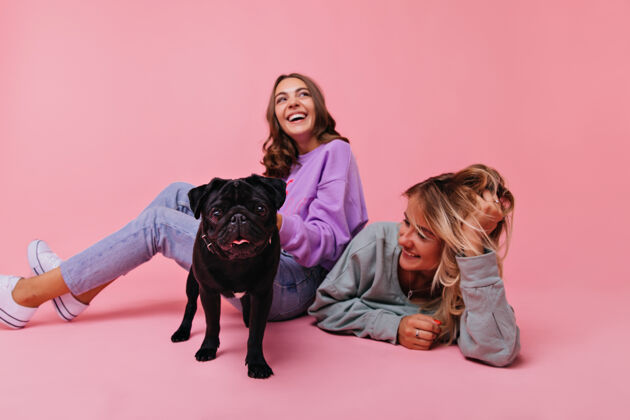 放松兴奋的黑发女孩坐在地板上与黑色斗牛犬两个女性朋友与可爱的宠物玩的室内肖像积极友谊时尚