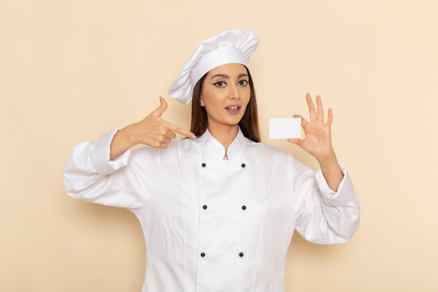 烹饪身穿白色厨师服的年轻女厨师正拿着塑料卡站在浅白的墙上举行人女性