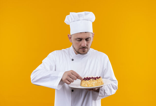 看着年轻帅气的厨师穿着厨师制服 拿着蛋糕看着盘子里孤立的橙色空间拿着盘子厨师