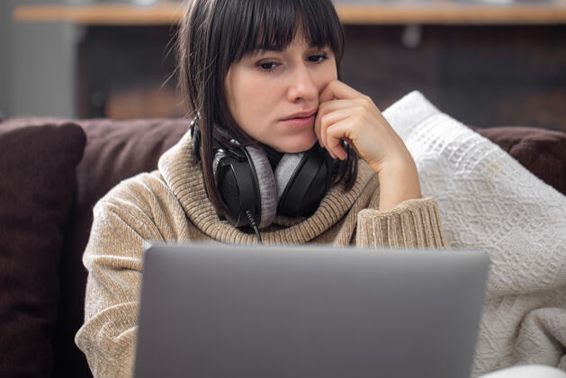 教育年轻漂亮的黑发女郎戴着耳机 穿着舒适的毛衣 看着笔记本电脑屏幕课程电话远程